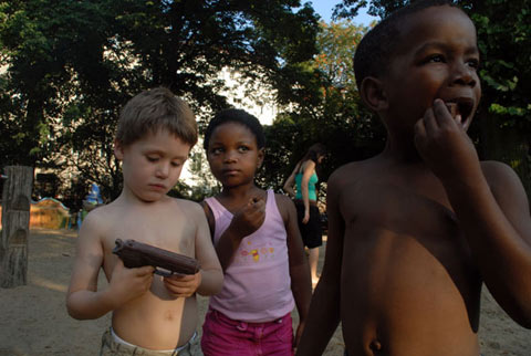 Photography of children on playground playing with a chocolate gun and eating it. By YLS Yvonne Lee Schultz
